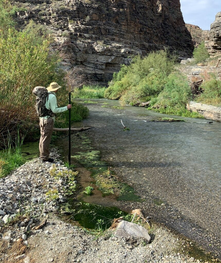 Eine Person wandert mit Rucksack in der Nähe eines Flusses durch die Natur