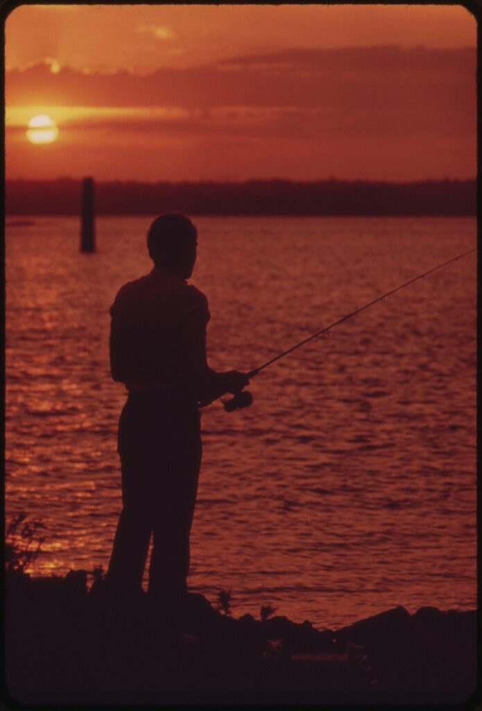 Ein Angler steht bei Sonnenuntergang nachdenklich am Seeufer