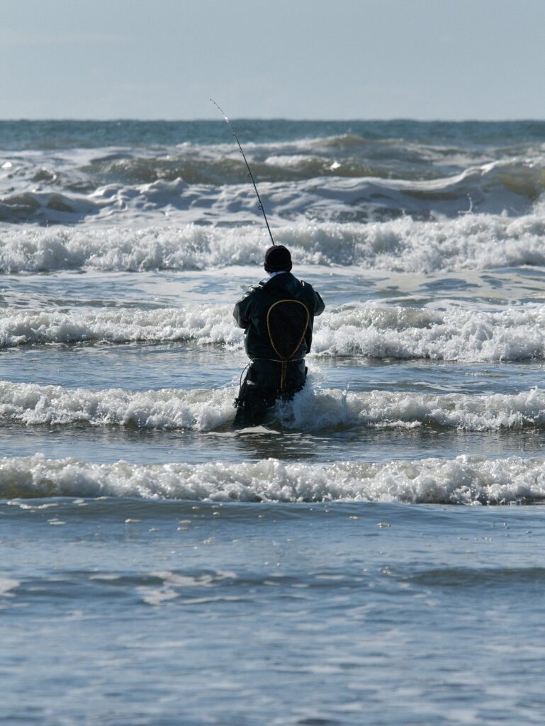 Angler beim Brandungsangeln am Sandstrand mit Wellen im Hintergrund